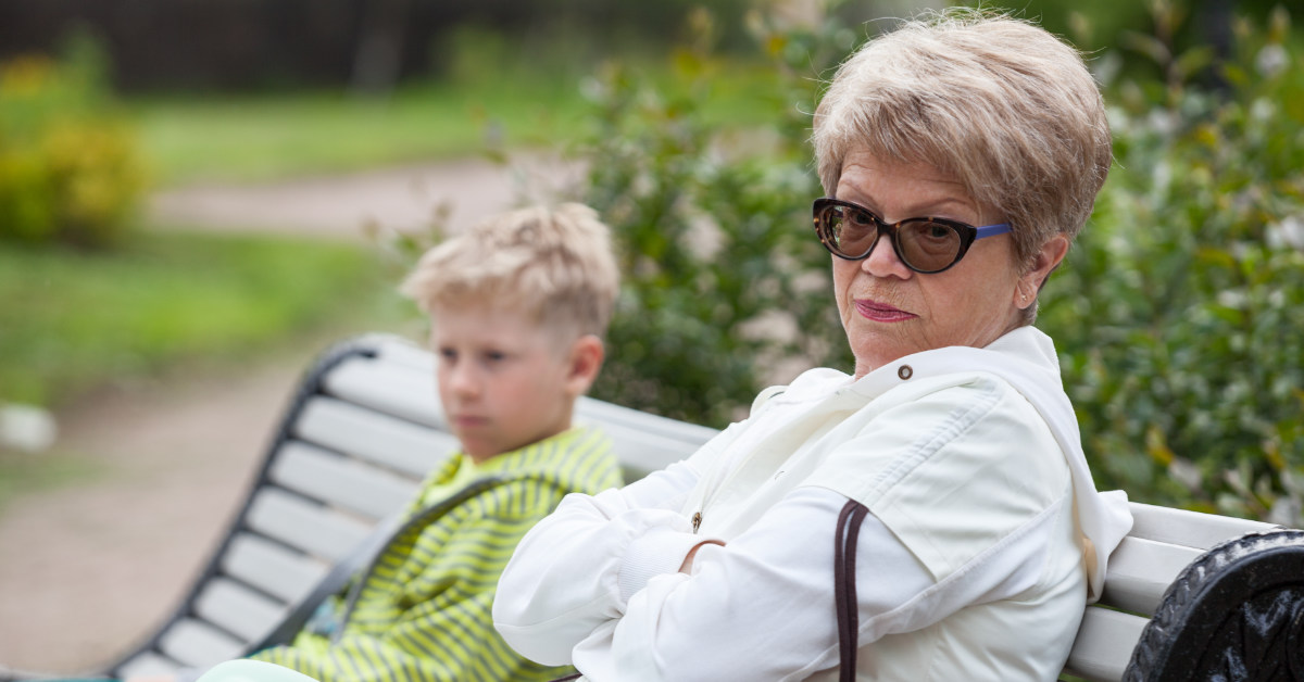 grandparent reluctantly sitting with grandchild on bench