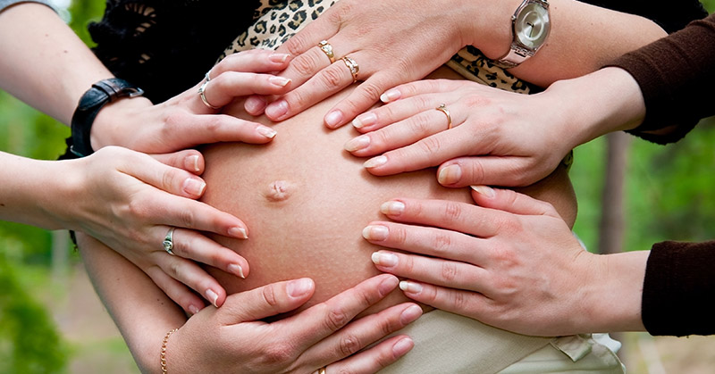 various hands placed on a pregnant woman's stomach