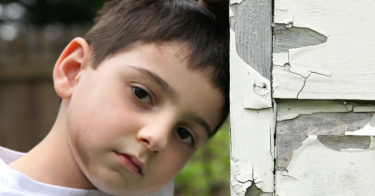 young boy leaning his head against the outside wall of a home