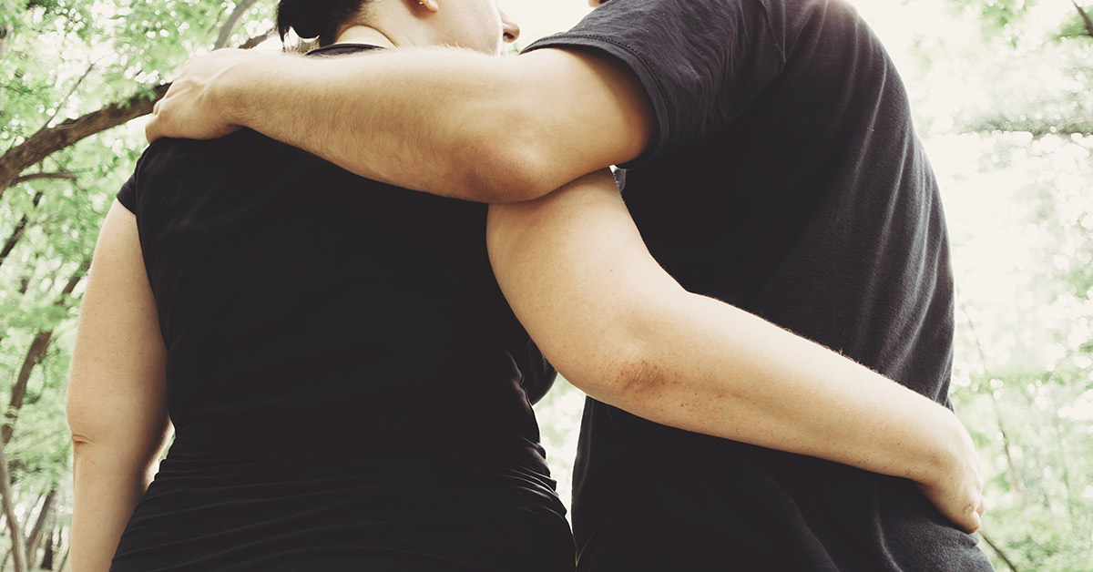 a couple seen from behind embracing. They are both wearing black shirts