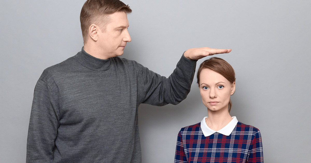 man placing hand over womans head to indicate he is tall and she is short