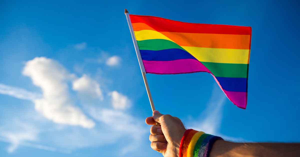 LGBTQ+ flag held with sky in background