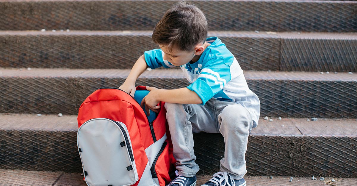 young boy packing a school bag on a set of stairs