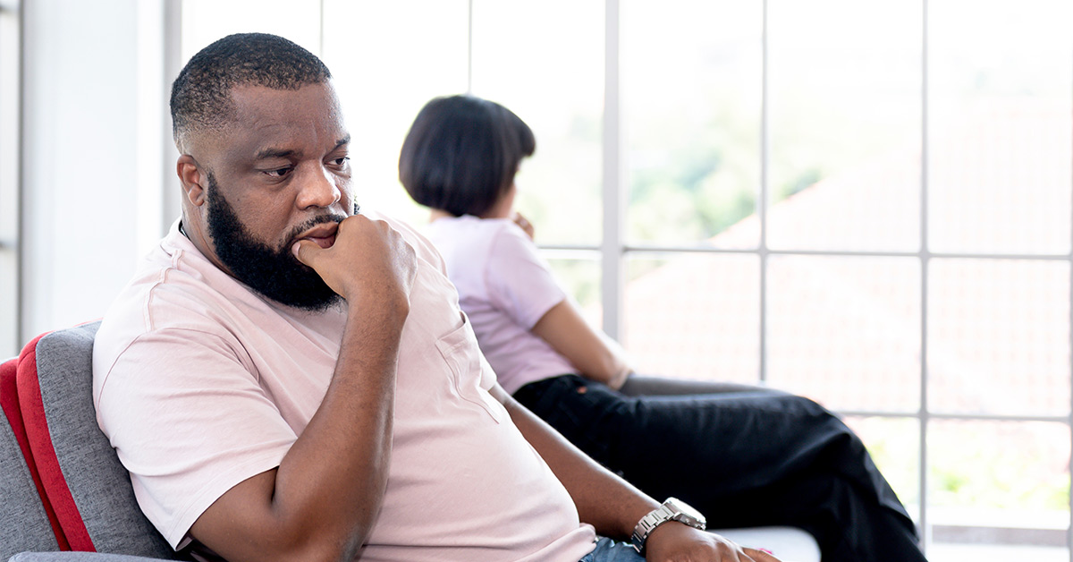 concerned man sitting on couch with partner who is turned away from him