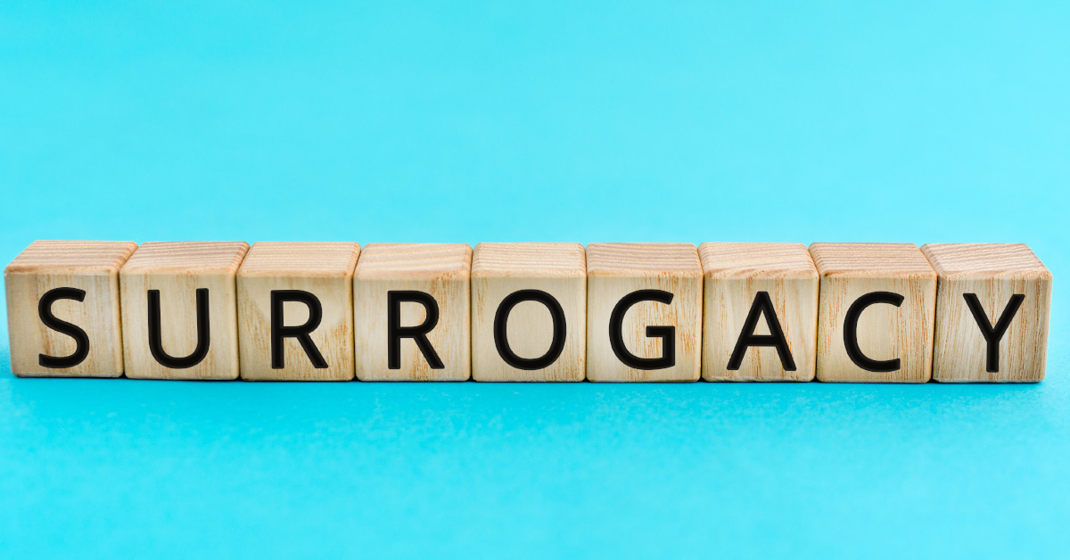 a sky blue background with wooden cube pieces with black letters spelling "surrogacy"