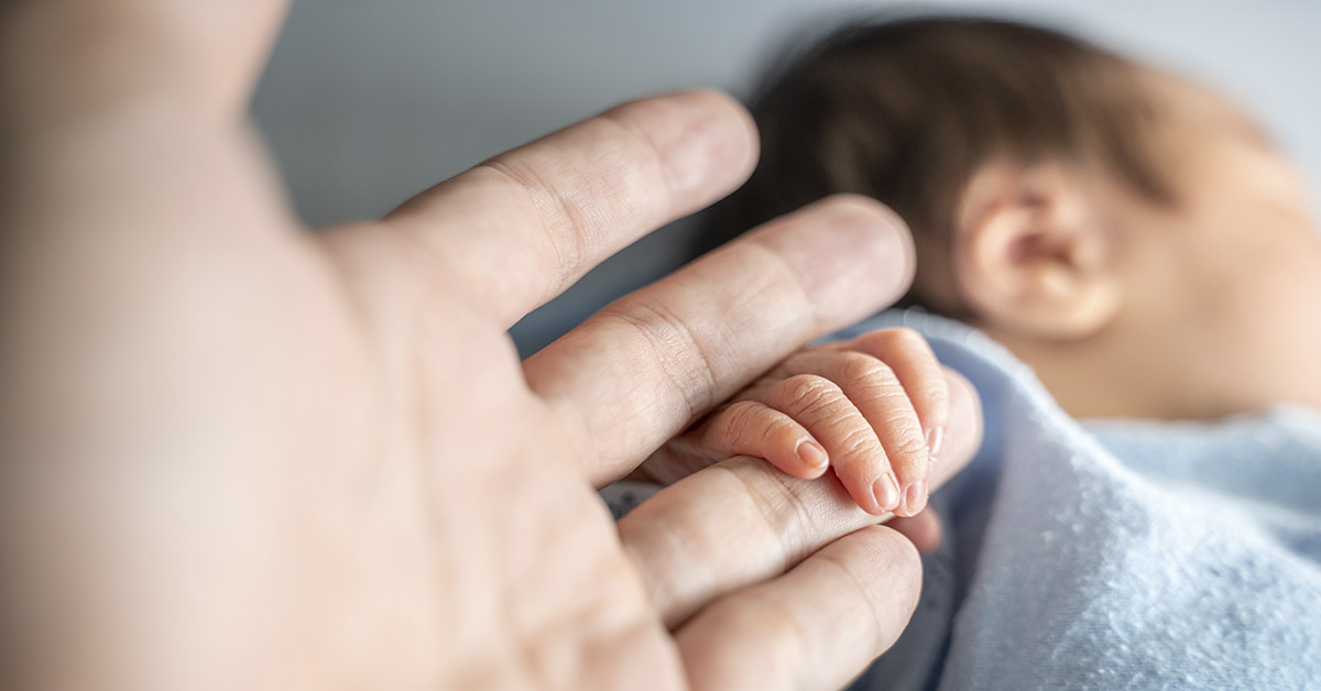 infant holding finger of adult hand