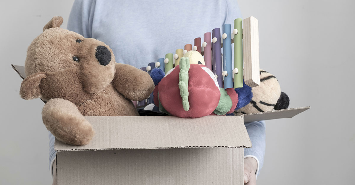person holding a cardboard box full of toys including a stuffed bear and xylophone