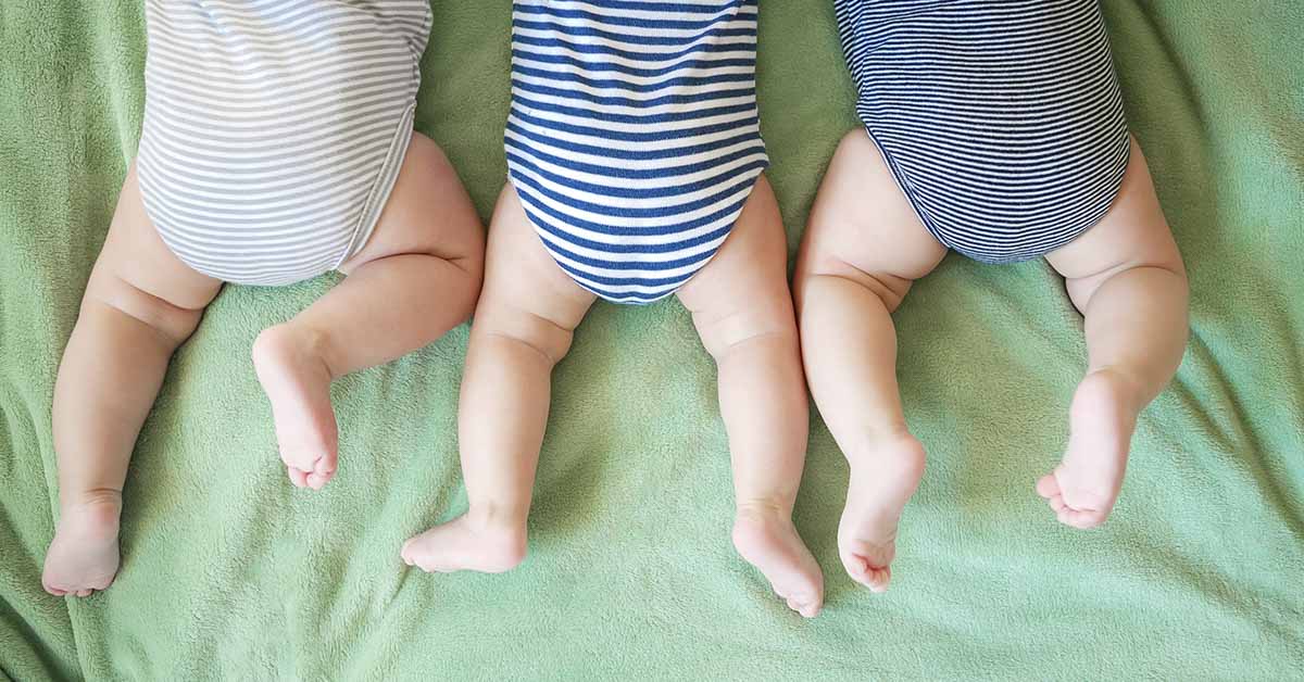 3 infants lying on their stomachs side by side on a green sheet