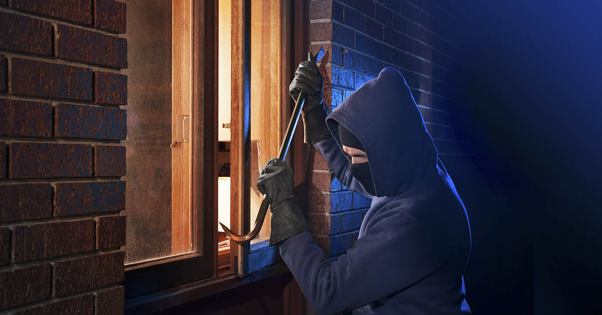 masked burglar attempting to jar open window with crowbar