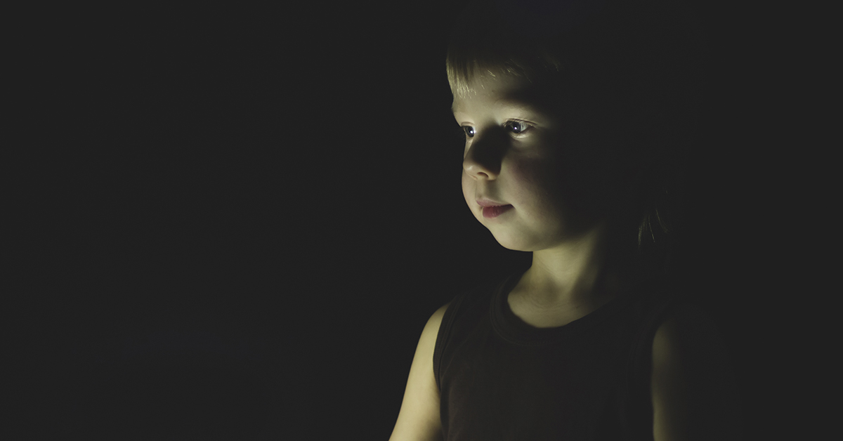 toddler in dark with face illuminated by what could be candle light