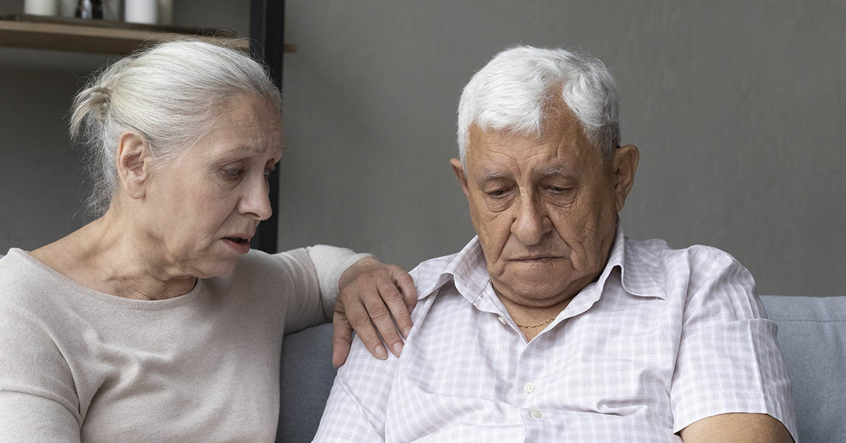 elderly couple. wife consoles husband and places hand on his shoulder